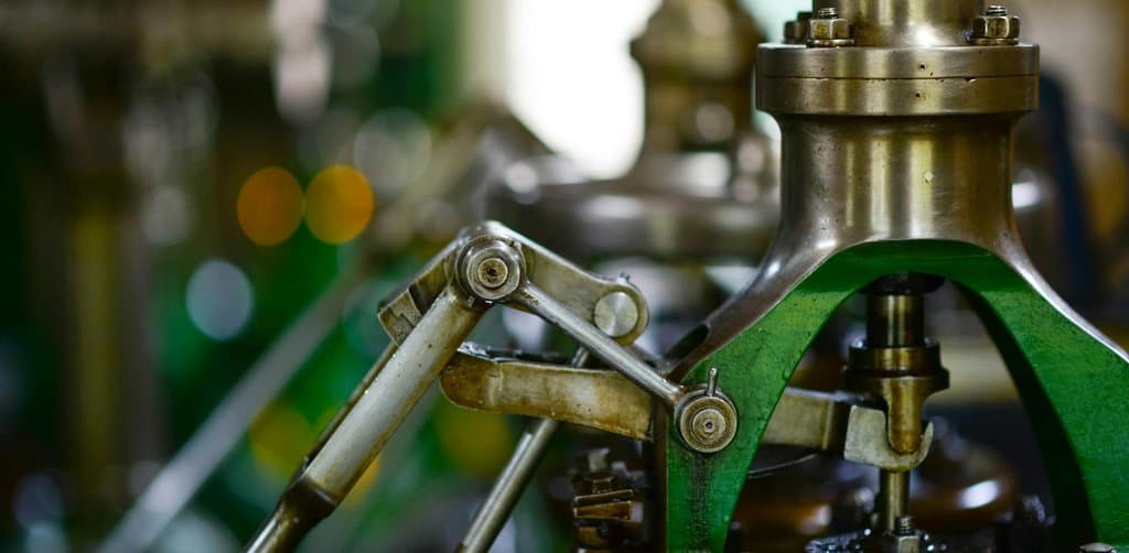 A close-up of polished brass and green-painted vintage industrial machinery with mechanical linkages and bolt-secured housings catching the light, the kind of hard asset that anchors the senior debt collateral package in how to finance a leveraged buyout LBO