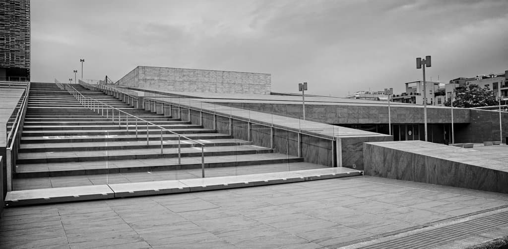 A black-and-white wide-angle view of a modernist concrete civic building with a grand external staircase and contemporary architectural geometry of large angular planes against a cloudy gray sky, the structural metaphor that captures how a deliberately designed seller financing structure carries the weight of the deal