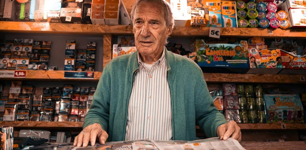 Small business owner standing behind the counter of a neighborhood newsstand, representing the kind of independent operator who often sells with owner financing