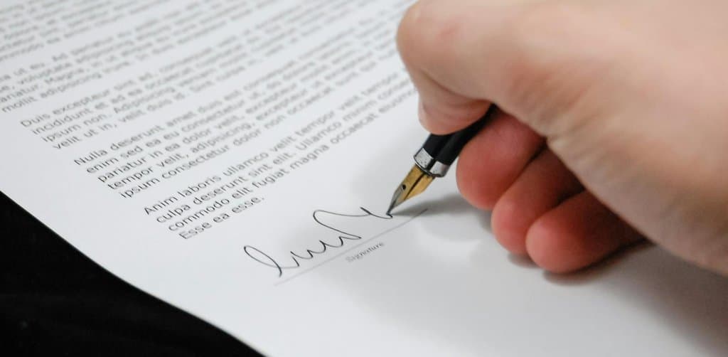 Hand signing a promissory note with a fountain pen, representing the formalization of a seller-carry obligation at closing