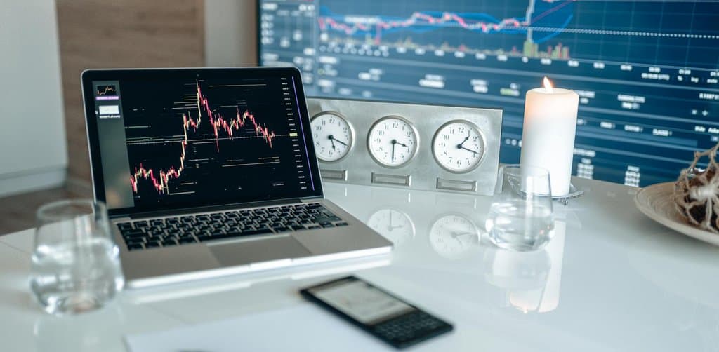 Trading desk with a candlestick chart on the laptop screen and a second monitor showing a large market chart, representing the public market alternative
