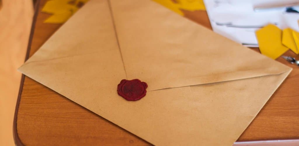 Brown kraft paper envelope with a deep red wax seal pressed onto the flap, resting on a wooden desk with paper scraps in the background, the symbolic 'deal sealed' moment of a fully executed seller-carry agreement after buying a business with seller financing