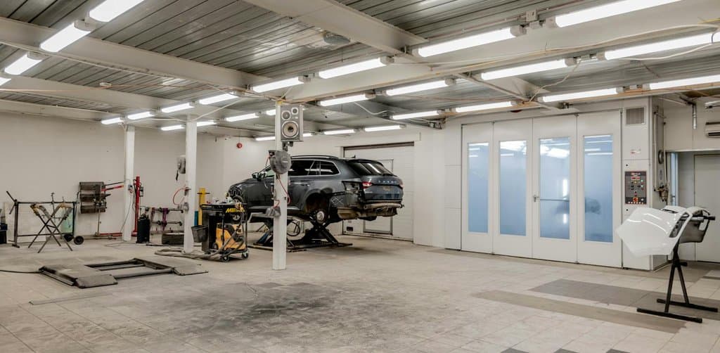 Modern auto repair shop interior with bright fluorescent lighting and a vehicle lifted on a service rack, the kind of operating small business that frequently changes hands through buying a business with seller financing