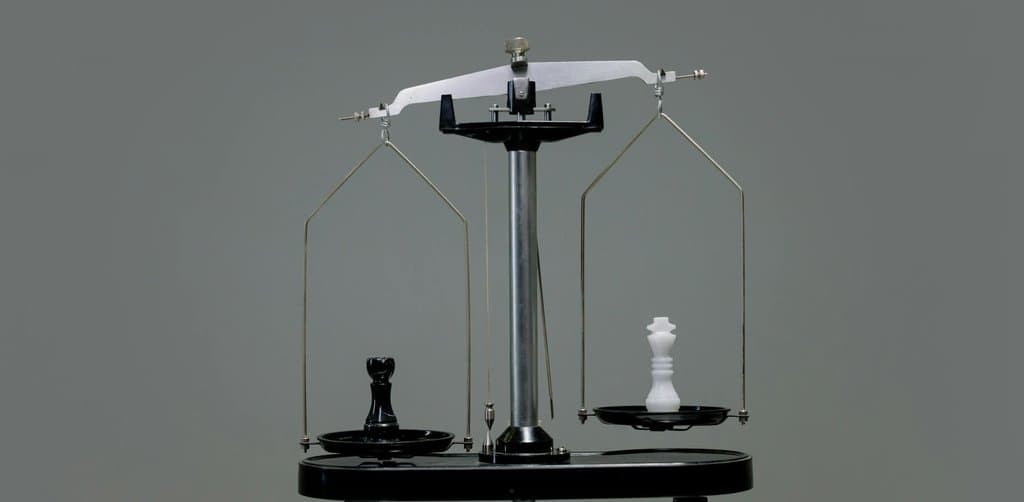 A black chess piece and a white chess piece balanced on a precision scale, representing the structural comparison between cash flow lending and collateral lending
