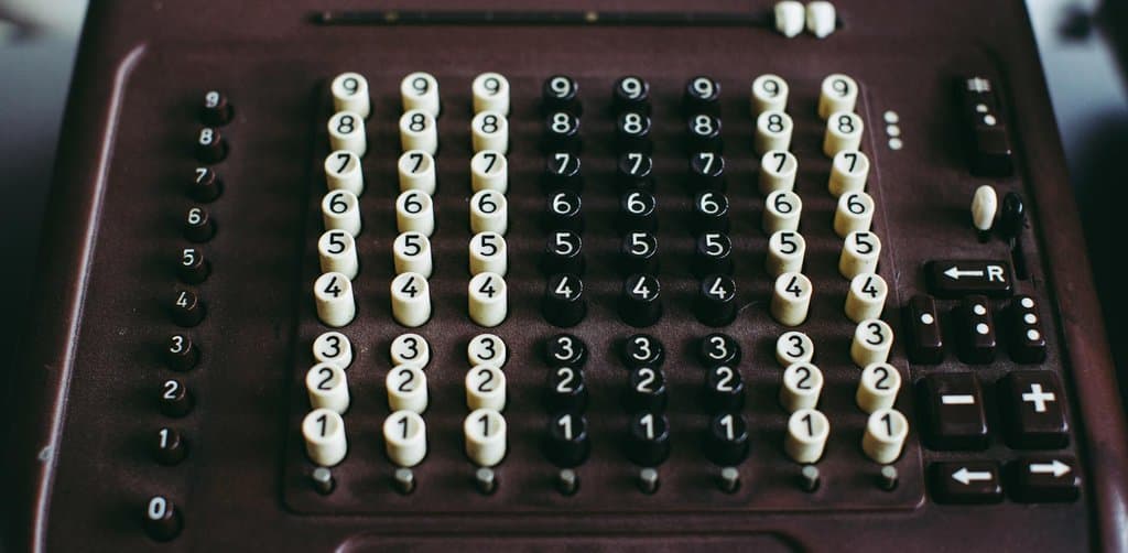 A close-up overhead view of a vintage Diehl mechanical adding machine with eight columns of cylindrical white and black numeric keys numbered 0 through 9 arranged on a deep maroon plastic body with smaller arrow control keys on the right side and a row of indicator buttons on the left edge, the analog calculation discipline that mirrors how careful annual esop valuation work runs through every variable in the company financials