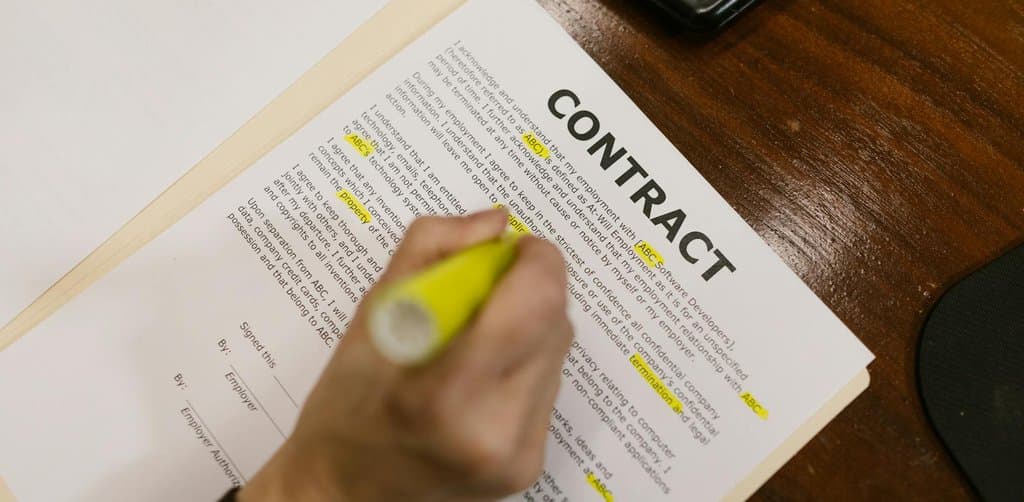 Hand using a yellow highlighter on a printed contract document with words like CONTRACT and ABC marked in yellow, the close-reading pass a buyer or attorney runs on every lien filing surfaced during pre-purchase diligence