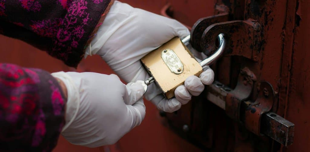 Gloved hands working a brass padlock on a rusty red door, symbolizing the unlock step in how to remove a business lien from public record