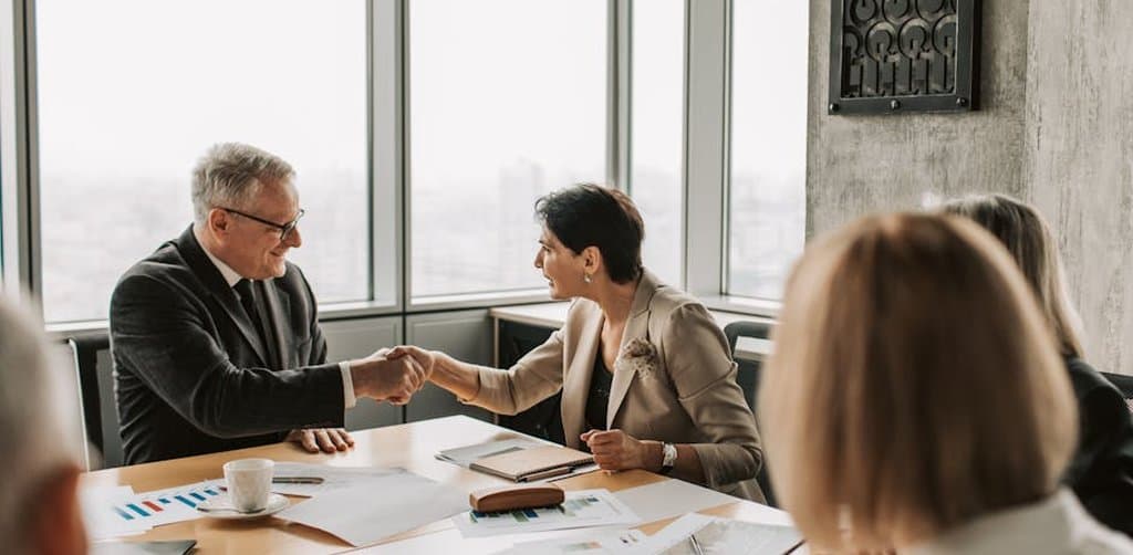 Business acquisition lenders meeting with a buyer to finalize loan terms during a formal handshake