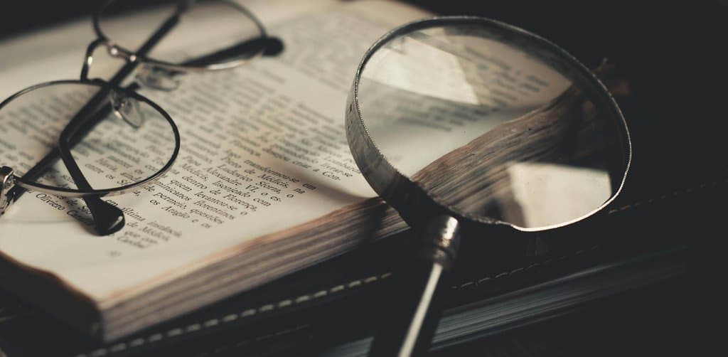 A round reading magnifying glass and a pair of round reading glasses resting on the open pages of a vintage Italian-language hardback book sitting on a stack of leather-bound notebooks, the close reading required to understand the new SBA loans 2025 program updates