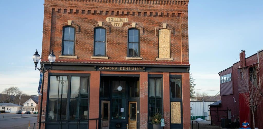 A restored two-story red-brick commercial building with H.H. Jewell 1880 inscribed at the top and a Wabasha Dentistry storefront on the ground floor, the kind of owner-occupied real estate that SBA 5(04) loans are built to finance