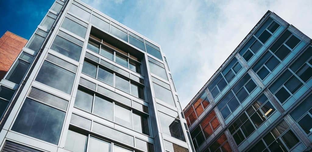 Two modern office buildings with extensive glass-and-steel facades captured against a partly cloudy sky from a low angle on the street, the kind of owner-occupied commercial real estate that frequently anchors an SBA 504 acquisition