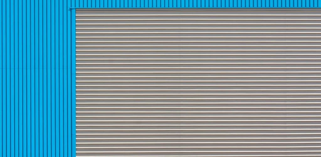 Close-up of bright blue corrugated metal warehouse cladding with a wide gray industrial roller door set into the lower portion, the kind of distribution or light-industrial property that frequently anchors a 504 acquisition