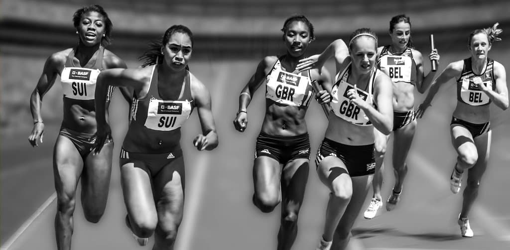 Female track athletes in black and white running a relay race with batons changing hands between team runners, a visual metaphor for the borrower handoff that defines SBA loan assumption rules