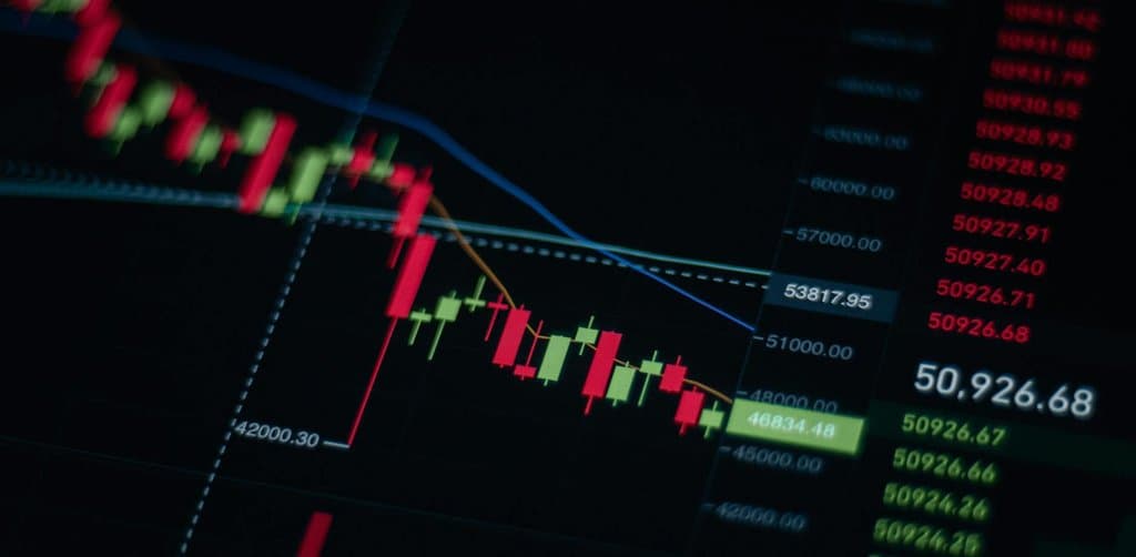 A dark stock chart screen with green and red candlestick bars showing a clear downward trajectory and falling price columns on the right side, the kind of financial deterioration that precedes most cases of SBA loan default