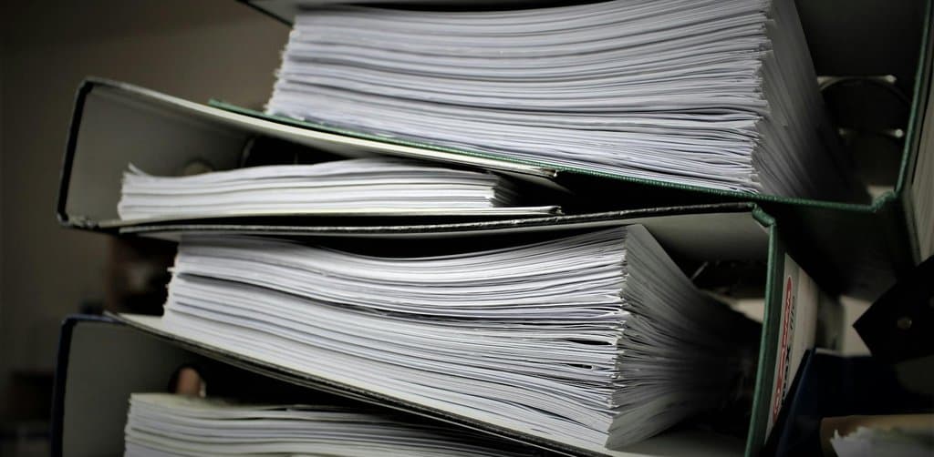 Three large black-spined ring binders stacked at angles, each crammed full of white printed pages with paper edges fanning out at the open ends, the loan documentation that gets pooled and tracked in the SBA loan lender secondary market