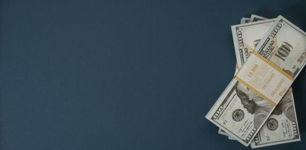 A neatly banded stack of one-hundred-dollar bills with a 10,000 currency band laid against a deep navy blue background, the kind of lump-sum cash injection a borrower considers when deciding whether SBA loan prepayment penalties make sense to absorb