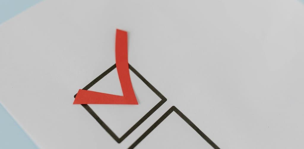 A bold red paper check-mark cutout placed inside a black-outlined square checkbox on a sheet of white paper resting on a light blue surface, the decision moment when an operator approves an SBA loan prepayment payoff