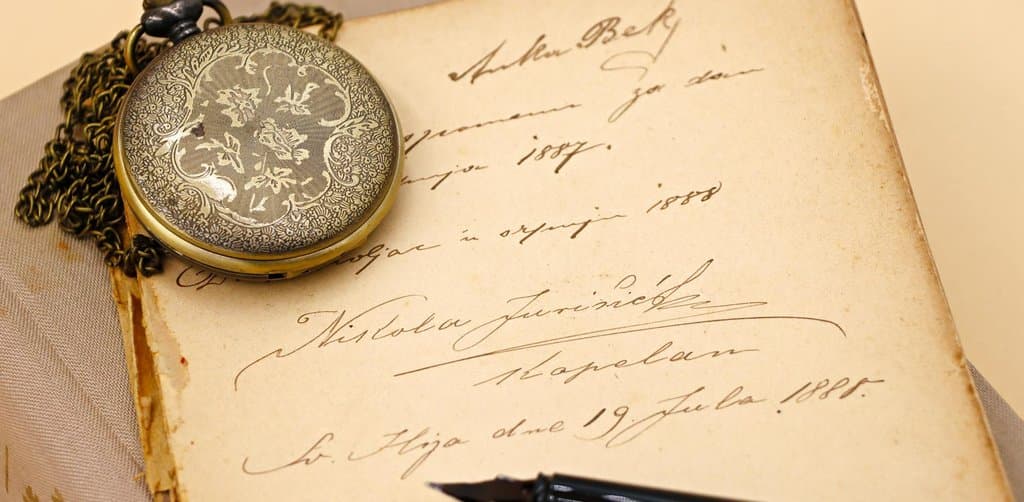 A vintage silver pocket watch with floral engraving resting on a handwritten ledger book page dated 1887 and 1888 with a fountain pen lying beside it, the historical version of the kind of promissory note paperwork that the SBA seller financing requirements regulate today