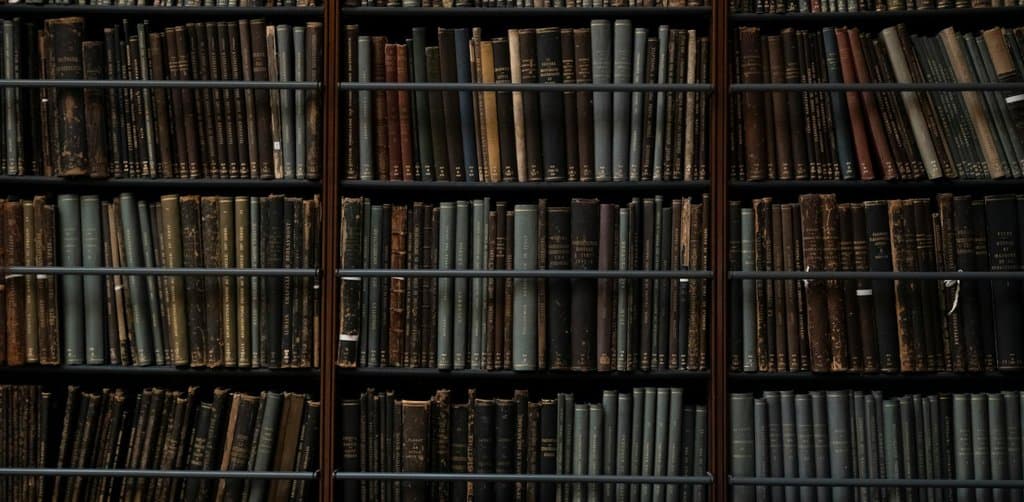 A wide view of a vintage law-library bookshelf with four full shelves of leather-spined hardback legal volumes packed tightly across multiple sections separated by dark wood dividers, the archive of historical SBA SOP versions and the regulatory framework around them