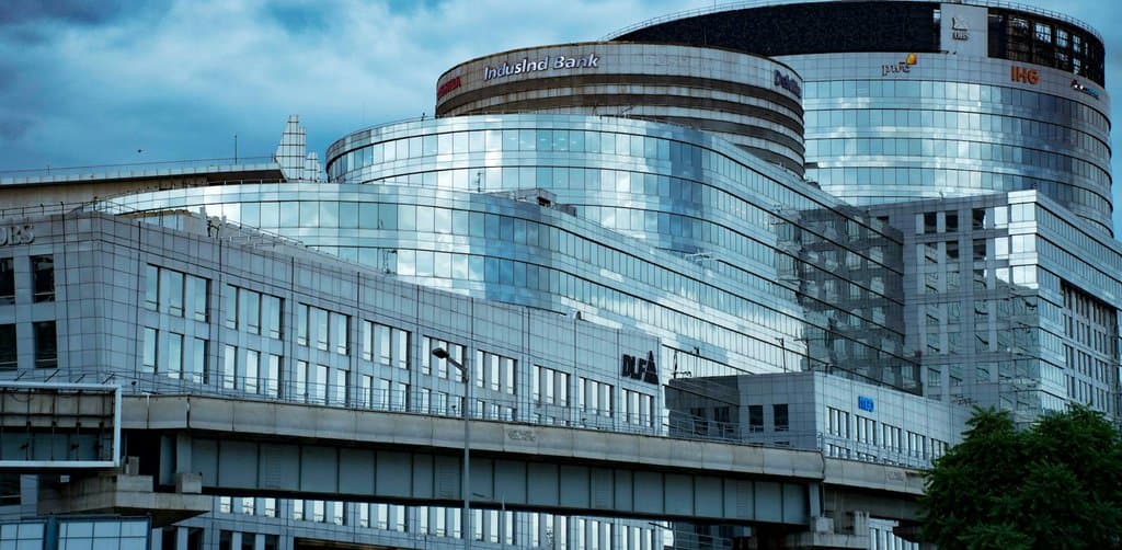 A tall reflective glass office building with multiple floors of windows under a stormy sky, the senior bank lender whose loan sits ahead of subordinated seller notes in the capital stack of a small business acquisition