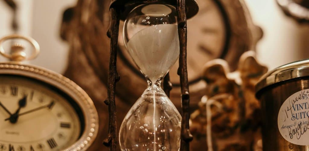 Vintage hourglass beside antique clocks, symbolizing the timeline that runs from filing through release of a business lien